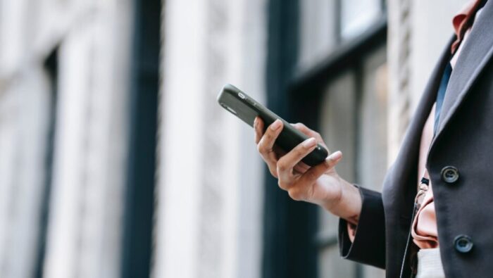 crop businesswoman messaging on smartphone while standing near building on street